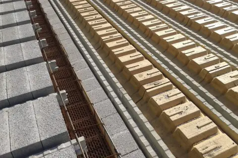 Budowa stropu DZ 3: betonowe pustaki i zbrojenie w rowkach, obok żółte pustaki szalunkowe.