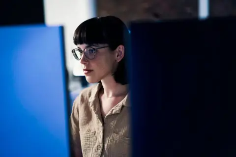 Junge Frau mit Brille und Kurzhaarschnitt, konzentriert auf einen Bildschirm. Sie repräsentiert eine der vielen Berufe mit Zukunft in der digitalen Welt.