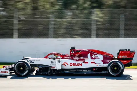 Biało-czerwony bolid Alfa Romeo F1 z numerem 7 pędzi po torze.