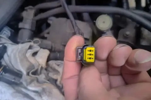 Wtyczka z żółtym wkładem, być może związana z błędem **dtc p1693 volkswagen**. W tle widać fragmenty silnika.