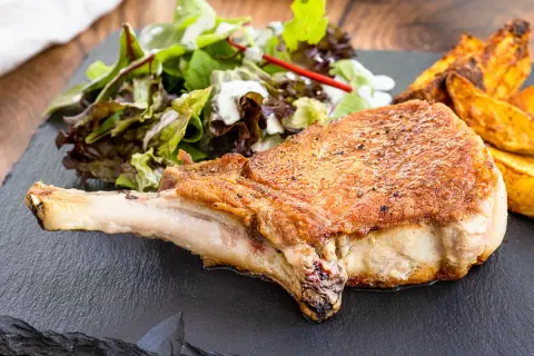 Saftiges Kotelett im Backofen, goldbraun gebraten, serviert mit knusprigen Kartoffelspalten und frischem Salat.