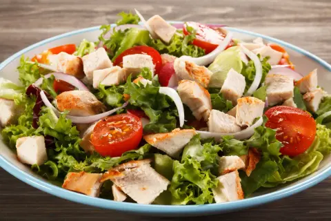 Insalata di pollo fresca con lattuga croccante, pomodorini succosi, cipolla rossa e pezzi di pollo grigliato.