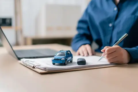 Osoba podpisuje dokumenty dotyczące wyrejestrowania pojazdu online. Obok leży model samochodu i kluczyki.