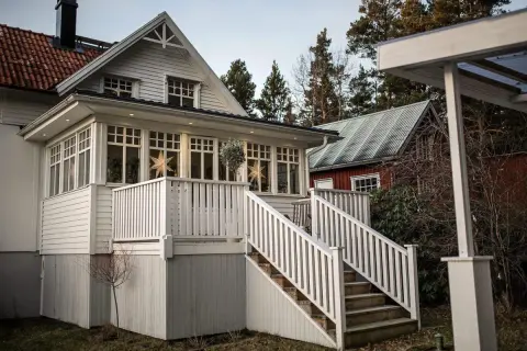 Vitt hus med glasveranda, stjärnor i fönstren och en röd stuga i bakgrunden. Glasveranda inspiration för ett mysigt hem.