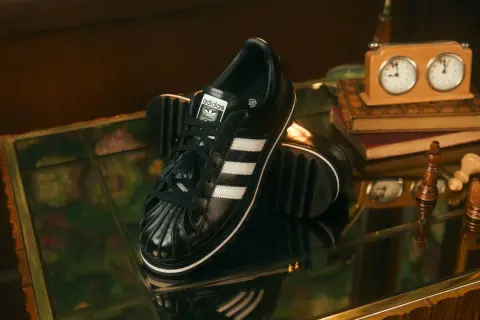 Schwarze Adidas Superstar Sneaker mit weißen Streifen, ein stilvolles Statement für aktuelle Sneaker Trends Herren. Schachfiguren und eine Spieluhr deuten auf eine strategische Eleganz hin.