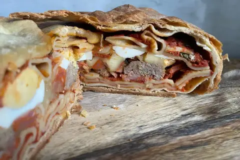 Fetta di timballo di pasta con strati di pasta, uova sode, ragù e carne, racchiuso in una crosta dorata.