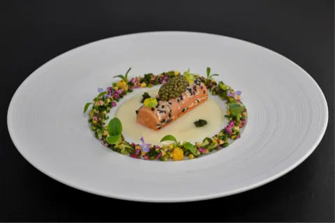 Un délicat pavé de saumon enrobé de sésame, surmonté de caviar, baignant dans une sauce onctueuse. Un plat qui pourrait faire partie d'un repas 7 services, orné de fleurs et de légumes croquants.