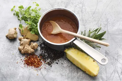 En kastrull med sötsur sås som på kinarestaurang, med ingefära, ananas, pepparkorn och chiliflakes.