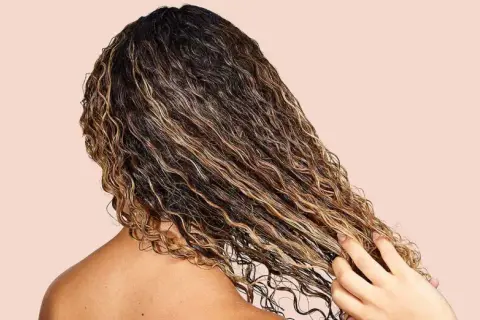Cabello rizado y húmedo con reflejos dorados, mostrando cómo fortalecer el pelo con productos nutritivos.