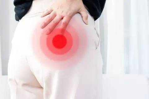 Person håller handen mot höften där en röd cirkel indikerar smärta, möjligen relaterad till piriformis triggerpunkt.