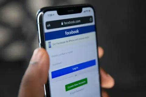Dłoń trzyma smartfon z ekranem logowania Facebooka. Szukasz sposobu, jak odzyskać konto na FB bez maila i telefonu?