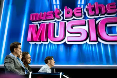 Trzech jurorów siedzi przed ekranem z napisem "must be the MUSIC".