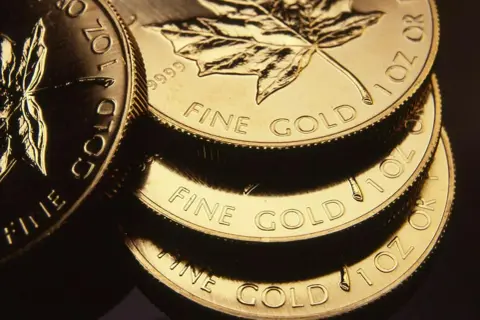 Stos złotych monet z liściem klonu i napisem "FINE GOLD".