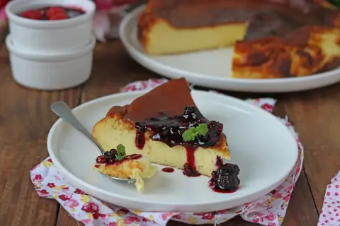 Una fetta di cheesecake basca cremosa, con topping di frutti di bosco e menta, su un piatto bianco.