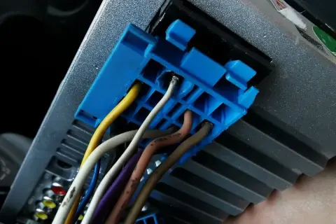 Niebieska wtyczka z przewodami, w tym żółtym i białym, podłączona do radia samochodowego. Prawdopodobnie część instalacji CAN bus.