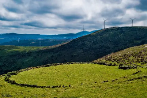 Prado das Chantas, un paisaje verde con molinos de viento en colinas onduladas bajo un cielo nublado.