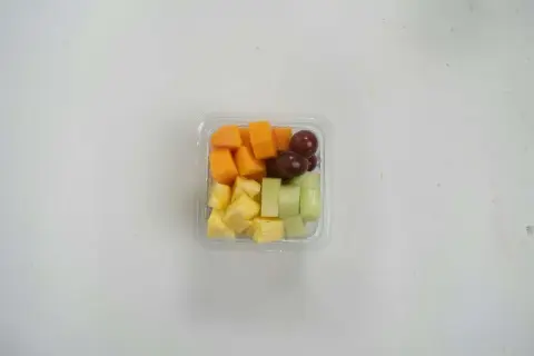 Pudełko z pokrojonymi owocami: ananas, melon, papaja i winogrona. Idealna przekąska, jeśli zastanawiasz się, czy mus owocowy można do samolotu.