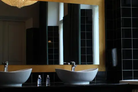 Elegante bagno nero design con due lavabi bianchi, rubinetteria cromata e specchio dorato. Pareti rivestite di piastrelle nere lucide.