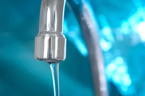 Grifo cromado con chorro de agua, indicando un buen bar presión de agua. Fondo azul brillante.