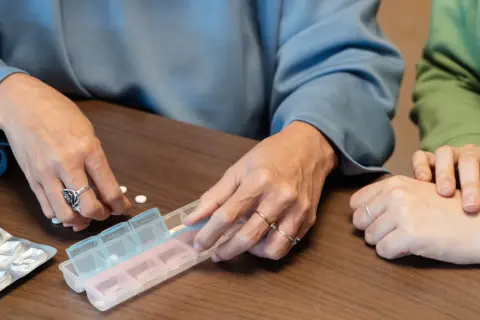 Dwie osoby sortują tabletki w pojemniku na leki. Dostępne są darmowe leki dla seniorów.