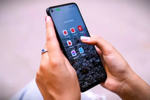 Dłoń z pierścionkiem na ekranie telefonu z ikonami aplikacji, w tym Messenger. Czy jak usunę wiadomość na Messengerze to on to widzi?