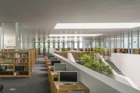 Nowoczesne wnętrze biblioteki Raczyńskich z rzędami regałów, komputerami i zielenią.