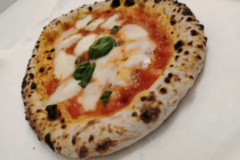 Une authentique pizza napolitaine, avec sa croûte gonflée et légèrement brûlée, garnie de sauce tomate, de mozzarella fondante et de feuilles de basilic frais.