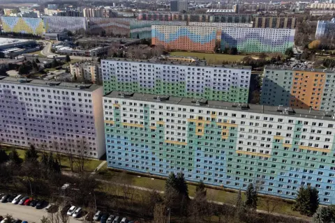 Kolorowe bloki z wielkiej płyty tworzą mozaikę na tle miasta. Długie, wielopiętrowe budynki pokryte są pastelowymi barwami: fioletem, zielenią, błękitem i pomarańczem.