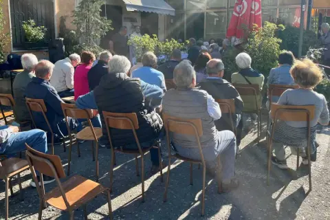 Un gruppo di persone ascolta un relatore durante un tricot cafè tutorial all'aperto.