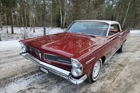 Röd Pontiac 60-tal, en klassisk bil med kromdetaljer, står parkerad i snöig skogsmiljö.