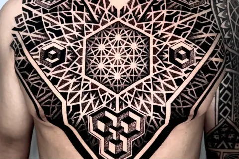 Ein komplexes Tattoo mit geometrischen Mustern bedeckt die Brust und den Arm. Es zeigt verschachtelte Hexagone, Würfel und stilisierte Dreiecke.