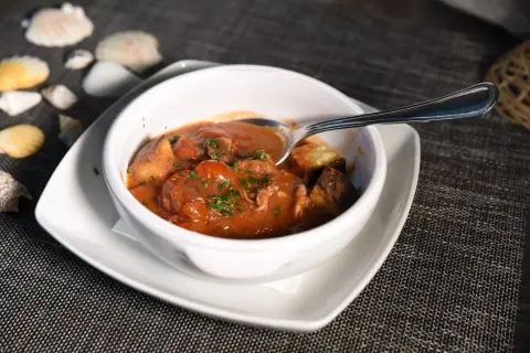 Polipetti in purgatorio, un piatto di mare con pomodorini e pane tostato, servito in una ciotola bianca su un tavolo scuro.
