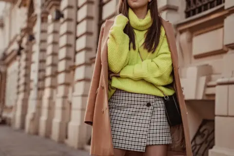 Modna stylizacja: neonowy sweter, płaszcz i spódnica w kratę.