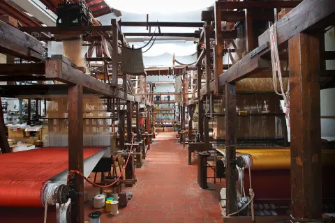 Interno di un antico setificio fiorentino con telai in legno e tessuti colorati.