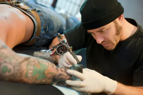 Artista de tatuajes concentrado, considerado el mejor del mundo, trabajando en un brazo con diseño detallado.