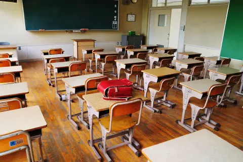 Pusta klasa z rzędami ławek i krzeseł, gotowa na lekcje w szkole dla dzieci z autyzmem. Czerwony tornister leży na jednej z ławek.