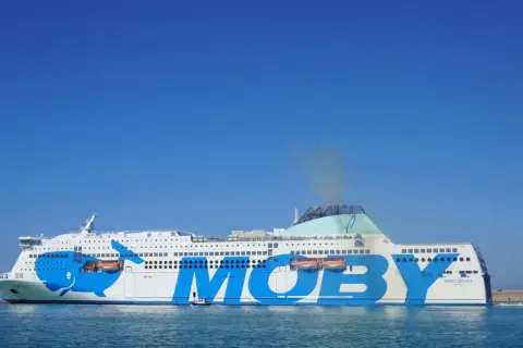 El ferry Moby Legacy, con su icónico diseño de ballena azul, navega rumbo a Cerdeña o Sicilia bajo un cielo despejado.