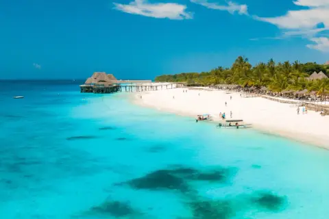 Rajskie zanzibar wakacje: biała plaża, palmy, turkusowa woda i drewniany pomost z domkami na wodzie. Idealne miejsce na relaks.
