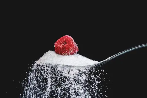Łyżka cukru z maliną, sugerująca, ile gram cukru dziennie jest bezpieczne.