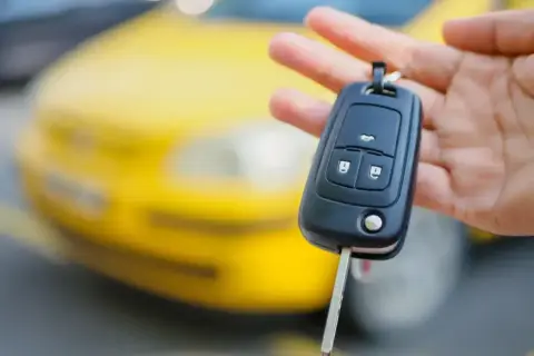 Kluczyk samochodowy z immobilizerem w dłoni, na tle żółtego auta.