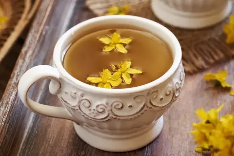 Aromaticzna herbata z dziurawca w ozdobnej filiżance, pływające żółte kwiaty dodają uroku.
