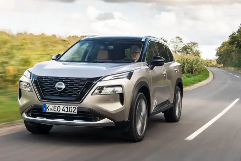 En man kör en beige Nissan X-Trail på en kurvig landsväg. Inga problem syns med bilen.