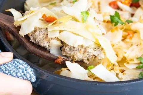 Ein Holzlöffel hebt eine Portion Krauttopf mit Hackfleisch aus einem Topf. Das Gericht ist im Ofen gebacken und mit Petersilie garniert.