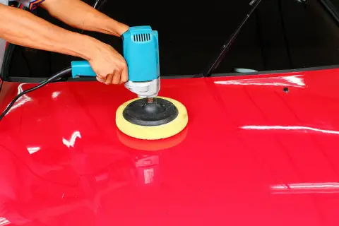 Mani che usano una lucidatrice blu per lucidare la macchina rossa, ottenendo una finitura brillante.
