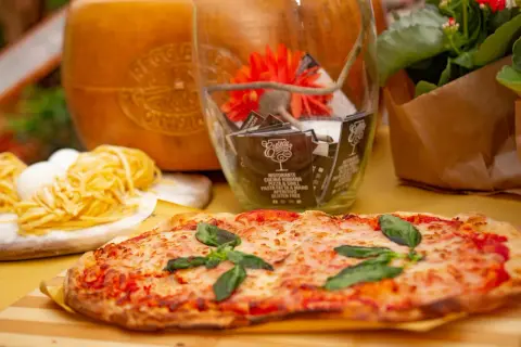 Pyszne rodzaje pizzy, makaron i ser parmezan. W tle szklany wazon z dekoracjami i kwiaty.