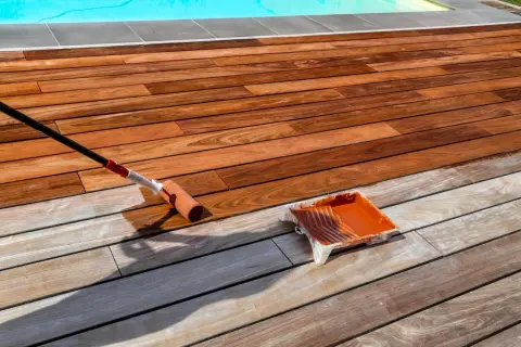 Application d'un saturateur sur une terrasse en bois exotique. Le rouleau dépose le produit, redonnant vie au bois.