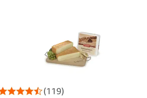 Due fette di formaggio tipo taleggio su tagliere di legno con uva e confezione.