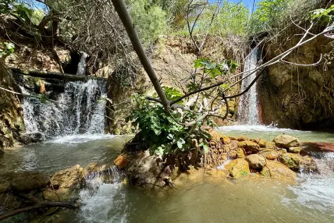 Cascada natural en las aguas termales Santa Fe, con rocas anaranjadas y vegetación exuberante.