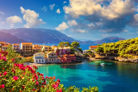 Piękna kefalonia pogoda czerwiec: kolorowe domki nad turkusową zatoką, góry w tle, kwitnące kwiaty na pierwszym planie.