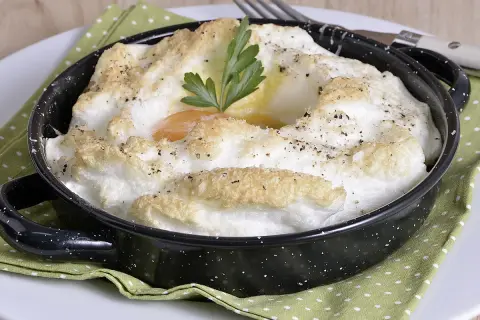 Delicioso huevo al horno, con clara montada y yema cremosa, adornado con perejil y pimienta.
